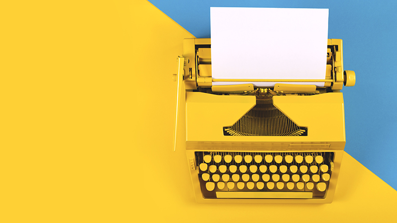Yellow bright typewriter on a yellow and blue background. Symbol for Copywriting